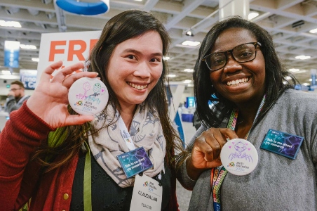 Two smiling female scientists holding custom designed buttons and wearing badges that say, "Talk to me about my research."