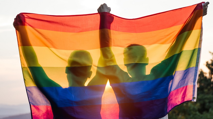 Two people hold up a Pride flag.