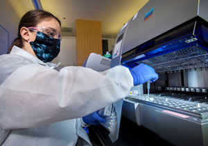 A medical laboratory scientist preparing a laboratory instrument, used to conduct real-time reverse transcription-polymerase chain reaction (RT-PCR) analysis of SARS-CoV-2 specimens.