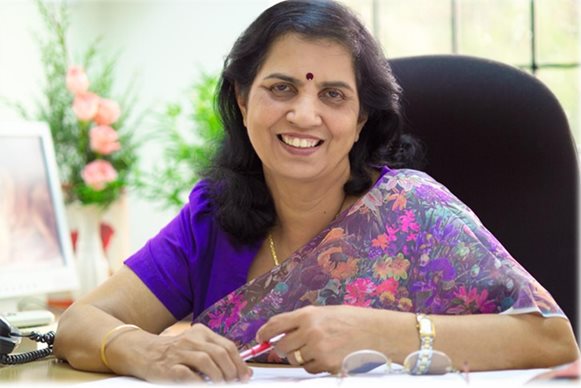 Suniti Solomon sitting at a desk and smiling at the camera.